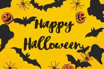 Happy Halloween text on bats, spiders, ghosts and pumpkins flat lay on yellow background. Happy Halloween greeting card, handwritten sign. Trick or treat!
