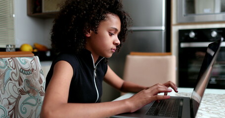 Preteen girl using laptop at home. Black child typing on computer