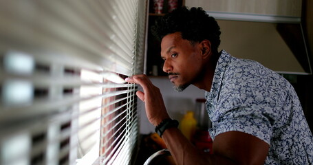 Suspicious man looking through window blinds