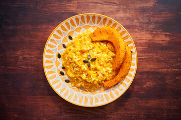 Pumpkin risotto with pumpkin strips and seeds photographed from above on a wooden background....