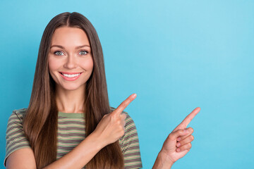 Photo of optimistic adorable cute girl with long hairstyle wear striped t-shirt directing empty space isolated on blue color background