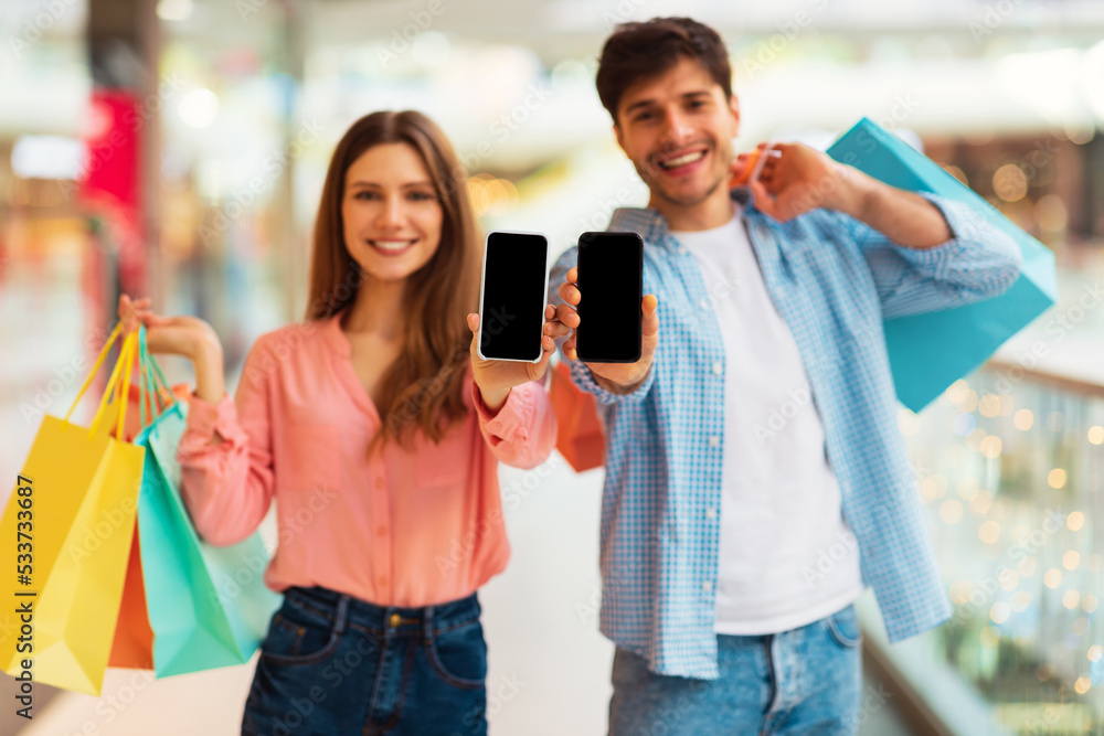 Poster cheerful couple showing smartphone screen recommending shopping application in hypermarket