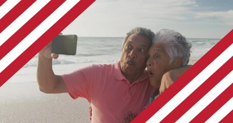 Animation of flag of united states of america over senior biracial couple taking selfie on beach - Powered by Adobe