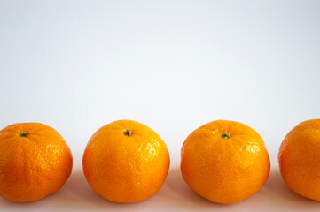Four tangerines lying in the foreground in a row. Orange fruits close up on a light background. Space for text