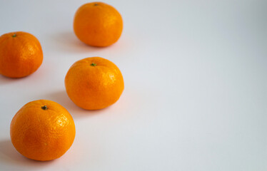 Four tangerines lying in a chaotic order on the left. Orange fruits on a light background. Space for text