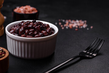 Black, canned beans in a white saucer against a dark concrete background