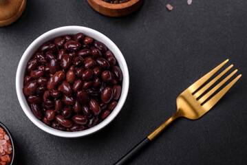 Black, canned beans in a white saucer against a dark concrete background