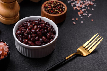 Black, canned beans in a white saucer against a dark concrete background