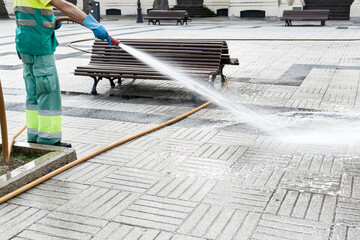 Worker cleaning a city square with water using a hosepipe. Public park maintenance concept. Copy space