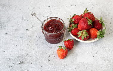 Homemade strawberry preserves or jam in a mason jar surrounded by fresh organic strawberries. Selective focus with blurred foreground and background.