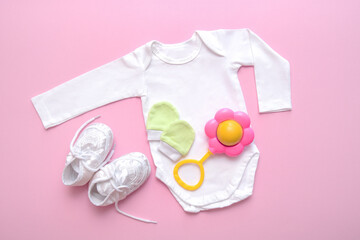 bodysuit for a newborn, booties, rattle, mittens on a pink background
