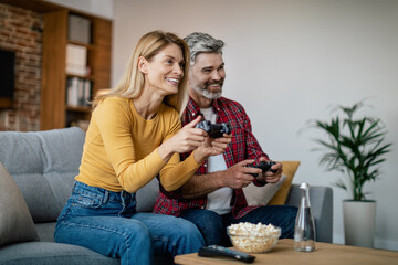 Laughing middle aged european couple with joysticks enjoy online game on computer, sit on sofa © Prostock-studio