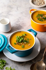 Pumpkin or butternut squash autumn creamy soup, blue bowl, grey background