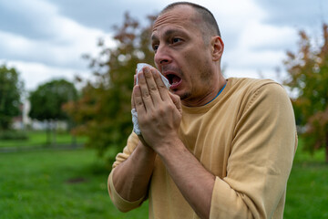 Allergic man blowing on wipe in a park on autumn season