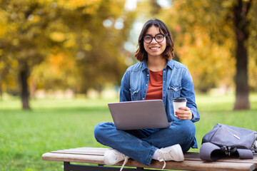 Smiling Young Middle Eastern Female Using Laptop And Drinking Coffee Outdoors