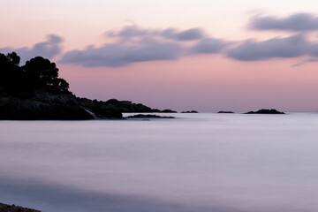 Amanecer en el mar con tonos lilas entre rocas y nubes