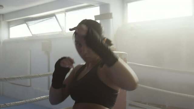 Female kickboxer fighting with hands and legs, handheld close up shot. Young strong fighter kickboxing, training in ring