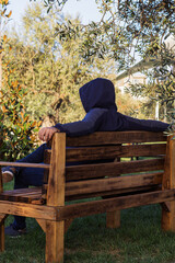 Fototapeta premium A man is resting on a wooden bench under an olive tree in the park.