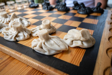 Traditional Georgian dish, khinkali Kalakuri, on wooden table, chess board, rustic, side view, black and light dough, playing chess. Selective focus, side view. Meat and cheese dishes