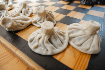 Traditional Georgian dish, khinkali Kalakuri, on wooden table, chess board, rustic, side view, black and light dough, playing chess. Selective focus, side view. Meat and cheese dishes