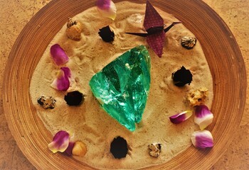 Holzschale mit Sand und roten und lila-weißen Blütenblätter mit türkisfarbenem großem...