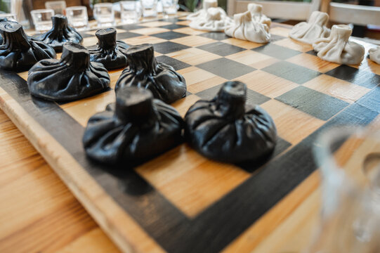Traditional Georgian dish, khinkali Kalakuri, on wooden table, chess board, rustic, side view, black and light dough, playing chess. Selective focus, side view. Meat and cheese dishes