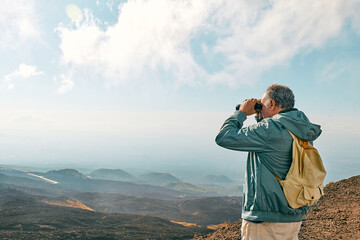 Rear view of man looking through binoculars at panoramic view of colorful summits of active volcano Etna, Tallest volcano in Continental Europe, Sicily, Italy.