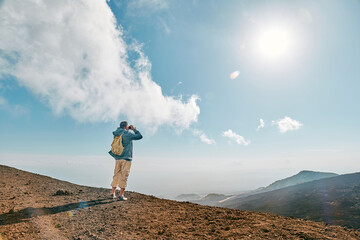 Rear view of man looking through binoculars at panoramic view of colorful summits of active volcano Etna, Tallest volcano in Continental Europe, Sicily, Italy. © Caterina Trimarchi