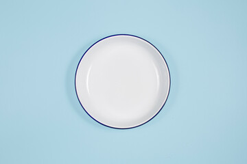 white plate in the center, top view, copy space. On a blue background - obrazy, fototapety, plakaty