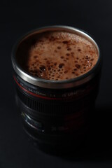 сappuccino coffee in a thermo cup in the form of a photo lens on a black background
