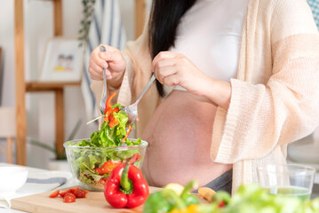 Obraz na płótnie Canvas Happy asian pregnant woman cooking salad at home, doing fresh green salad, eating many different vegetables during pregnancy, healthy pregnancy concept.