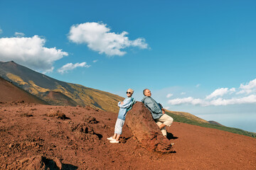 Happy tourist woman and man enjoying freedom, while admiring panoramic view of colorful summits of active volcano Etna, Tallest volcano in Continental Europe, Sicily, Italy.