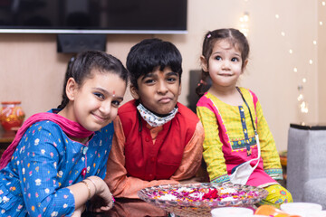 3 Indian kids, brother and sister friends siblings dressed up in ethnic wear smiling looking at the...
