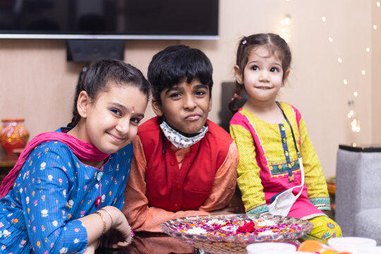 3 Indian Kids, Brother And Sister Friends Siblings Dressed Up In Ethnic Wear Smiling Looking At The Camera Celebrating Diwali Hindu Festival Laxmi Poojan With Ambient Light Bokeh