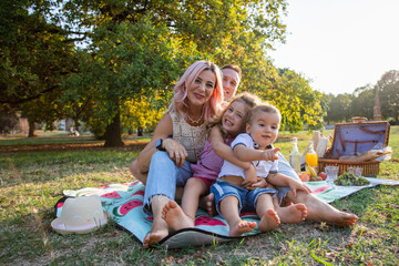 Family of four sitting on picnic mat in park having vegetarian picnic on a Sunny day