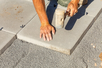 Worker with paver's dressing hammer places the tile exactly at the bed of small paving stones