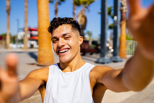 Young hispanic man 20- 25 years old smiling happy looking to the camera outdoors taking selfie on smartphone camera at summer beach