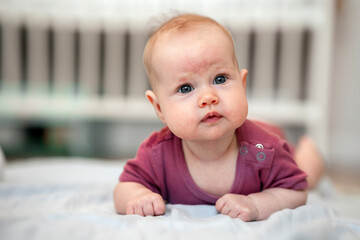 Close-up portrait of a cute Caucasian newborn baby. Charming funny baby baby looking into the camera. An authentic childhood and a candid lifestyle moment.