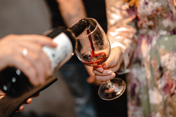 Closeup of a man's hand pouring red wine into a glass of a woman