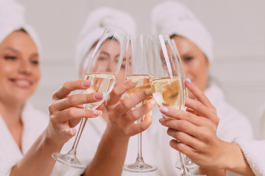 A group of women spend leisure time. Young attractive females in bathrobes drink champagne and chat merrily.