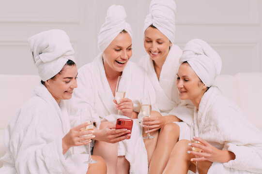 A group of women spend leisure time. Four Young attractive women in bathrobes look at the smartphone screen and smile.