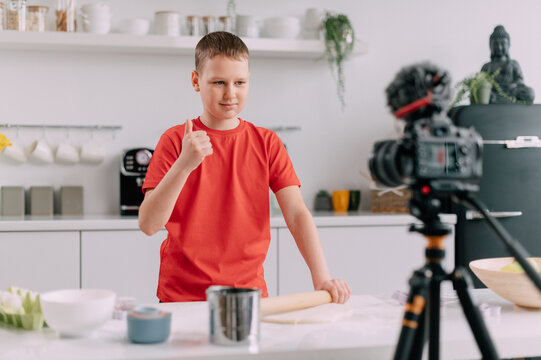 A child blogger makes a tutorial video at home. The boy shows a thumbs up at the camera.