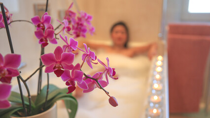 Beautiful flowering orchid with pretty young lady relaxing in nice bubble bath