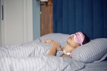 woman in a pink eye mask lies under a blanket in a bed and suffers from insomnia.