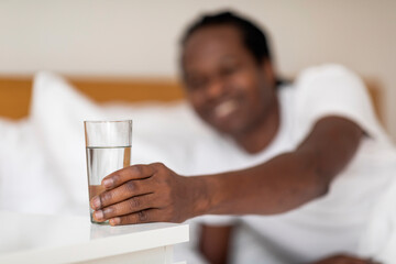 Black Smiling Man Taking Glass With Water From Bedside Table In The Morning