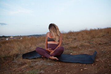 Naklejka na ściany i meble Pregnant woman makes yoga exercise outdoor in the meadow dry grass