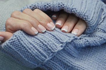 Beautiful manicure close-up on the background of a warm knitted sweater. Winter manicure. Women's well-groomed hands with salon French manicure.