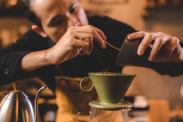 Fototapeta na wymiar hipster barista making a drink coffee with drip or filter style by pouring hot water to brew a caffeine beverage from black bean in cafe restaurant business shop, using paper for aroma to a cup or mug