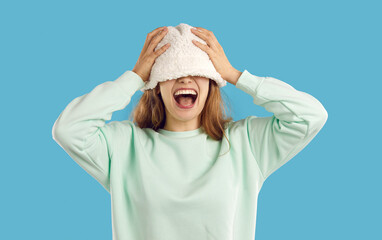Funny happy positive joyful young woman or teenage girl laughing as she covers her eyes with warm white fluffy fuzzy artificial teddy lamb wool bucket hat that she puts on her head. Fashion concept - obrazy, fototapety, plakaty