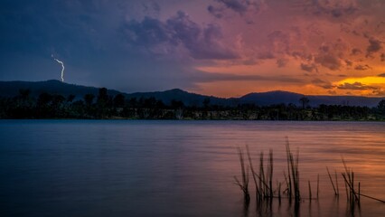 Beautiful panoramic shot of a lake under a cloudy sky with a lightning strike during the sunset